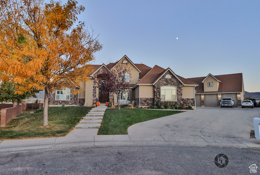 View of front of home featuring stone siding, a front yard, driveway, stucco siding, and a garage