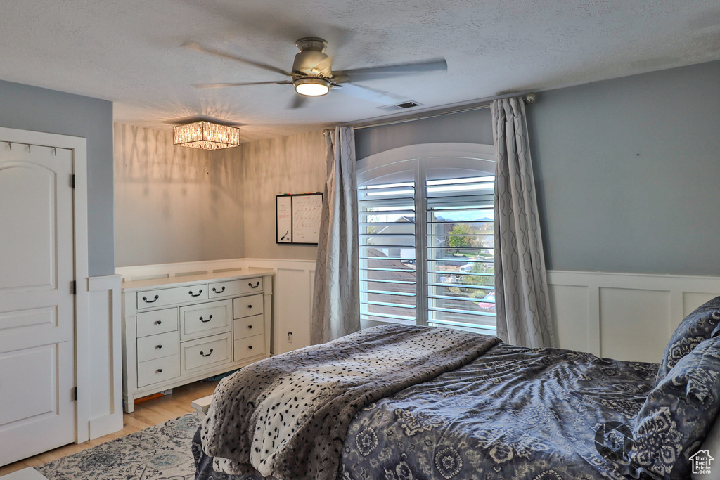 Bedroom with a decorative wall, a wainscoted wall, light wood-type flooring, and ceiling fan