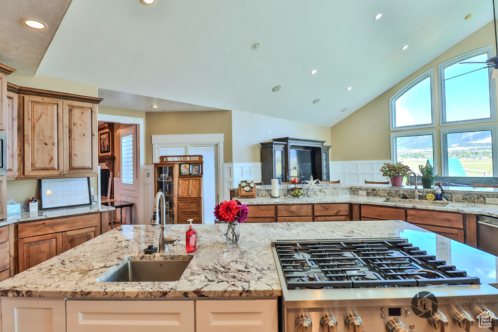 Kitchen with a sink, stainless steel gas cooktop, light stone counters, high vaulted ceiling, and recessed lighting