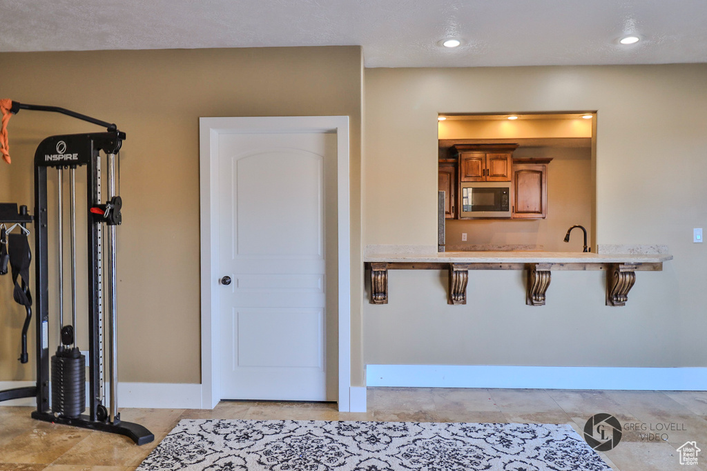 Kitchen with black microwave, brown cabinetry, baseboards, light countertops, and a kitchen bar