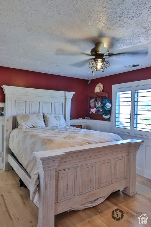 Bedroom featuring light wood finished floors, a textured ceiling, ceiling fan, and a wainscoted wall