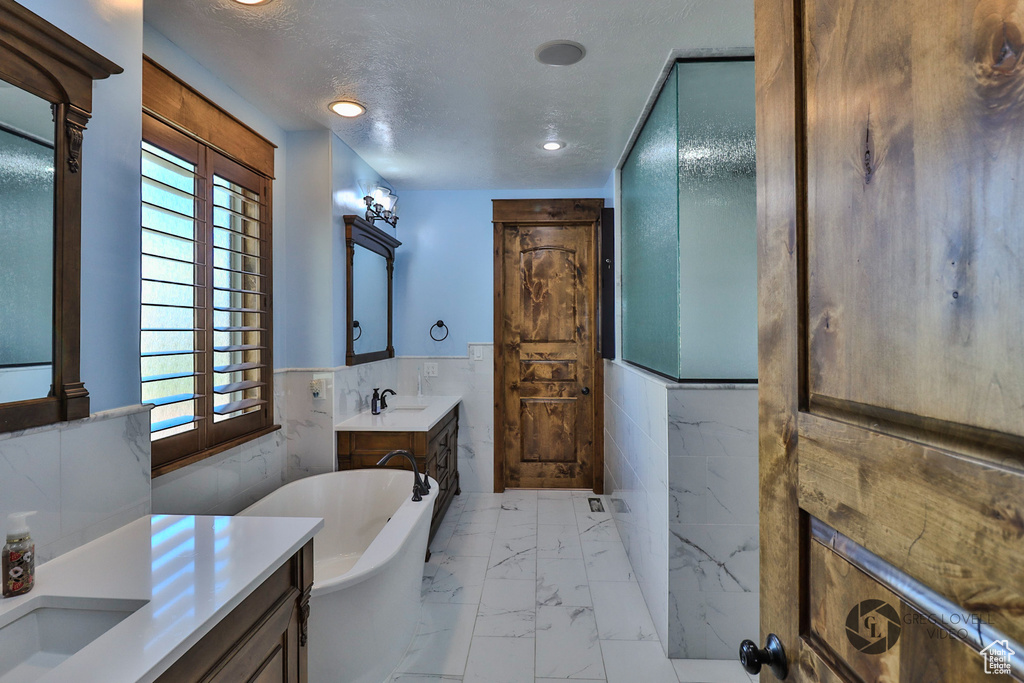 Bathroom featuring marble finish floors, tile walls, vanity, a freestanding bath, and wainscoting