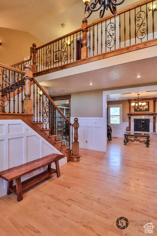 Staircase featuring a chandelier, wood finished floors, a decorative wall, a wainscoted wall, and high vaulted ceiling