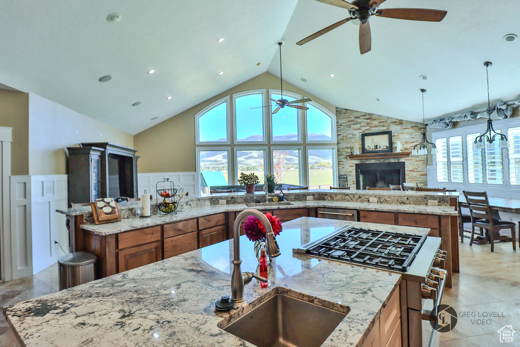 Kitchen with stainless steel appliances, a ceiling fan, a sink, brown cabinetry, and high vaulted ceiling