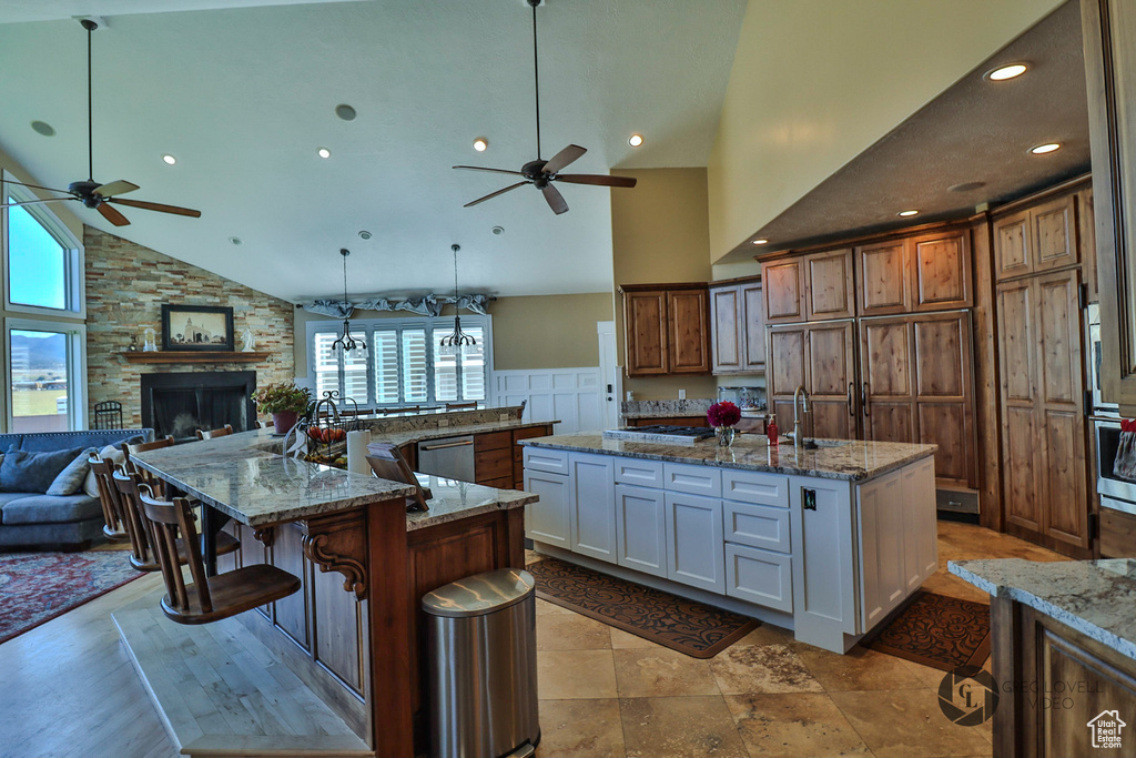 Kitchen with a ceiling fan, a spacious island, high vaulted ceiling, open floor plan, and a stone fireplace
