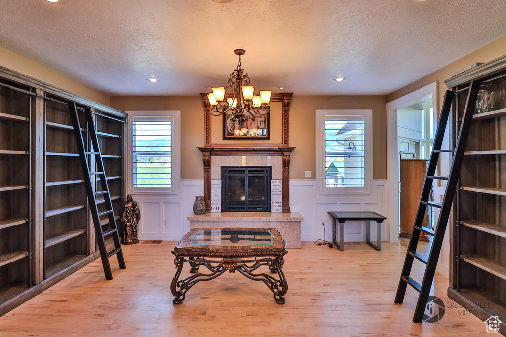 Living room featuring light wood-type flooring, wainscoting, a textured ceiling, a chandelier, and recessed lighting