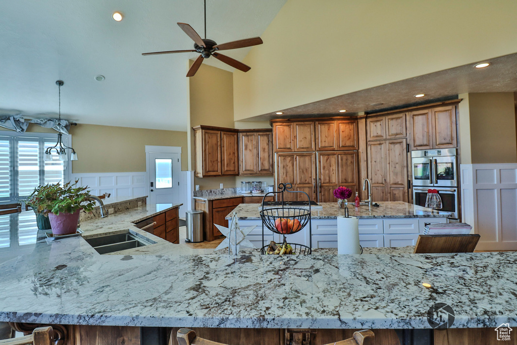 Kitchen with a large island, a ceiling fan, brown cabinets, high vaulted ceiling, and a sink
