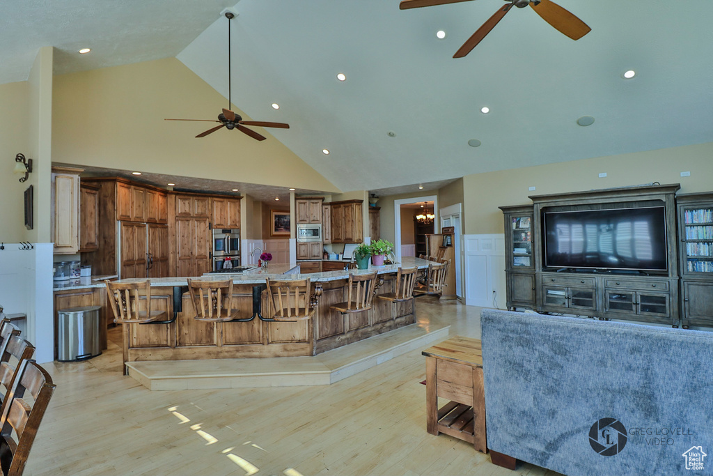 Kitchen featuring a ceiling fan, brown cabinets, stainless steel microwave, high vaulted ceiling, and light wood finished floors