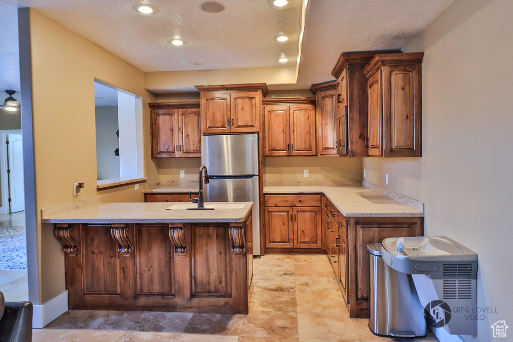 Kitchen featuring freestanding refrigerator, light countertops, a peninsula, brown cabinetry, and recessed lighting