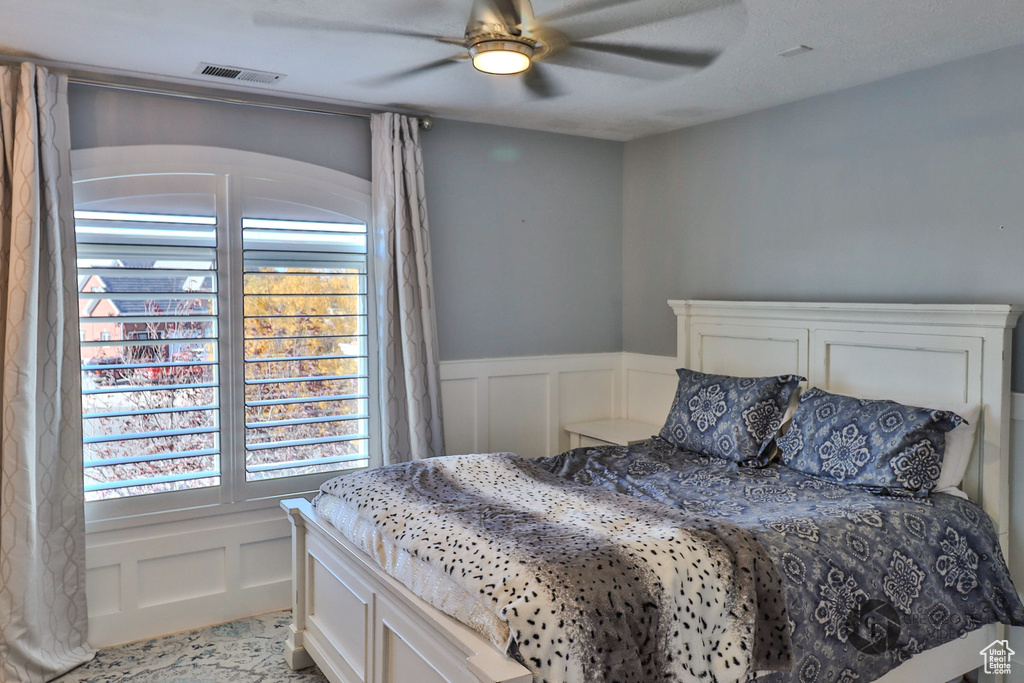 Bedroom with a decorative wall, multiple windows, wainscoting, and ceiling fan