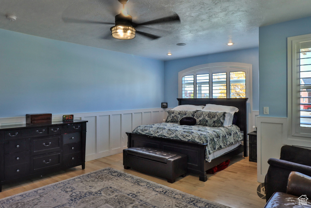 Bedroom with a wainscoted wall, light wood-style floors, ceiling fan, a textured ceiling, and a decorative wall