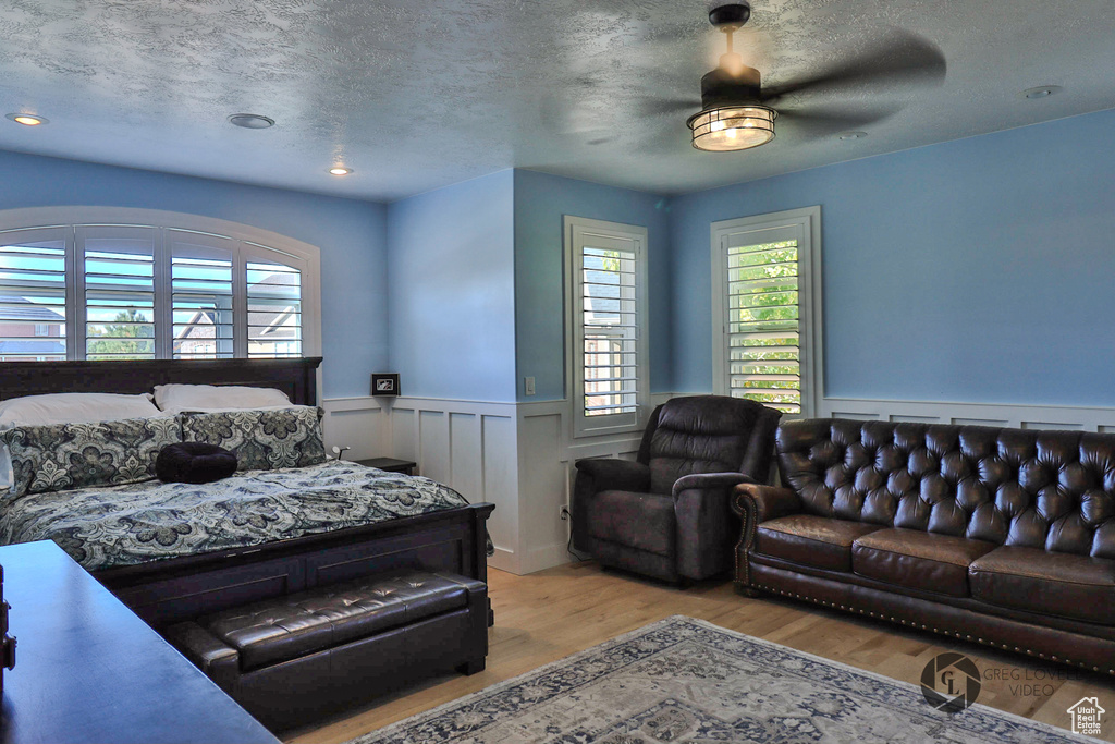 Bedroom with a wainscoted wall, wood finished floors, a textured ceiling, and ceiling fan