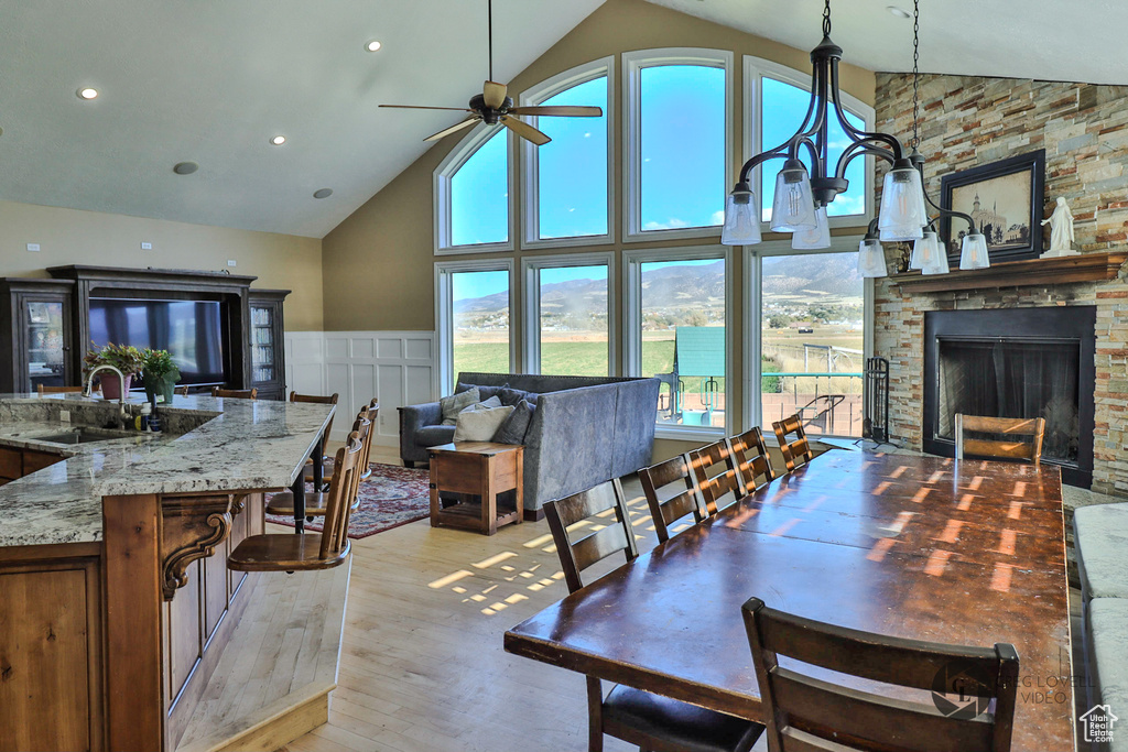 Dining area featuring high vaulted ceiling, light wood-style floors, a ceiling fan, a fireplace, and recessed lighting