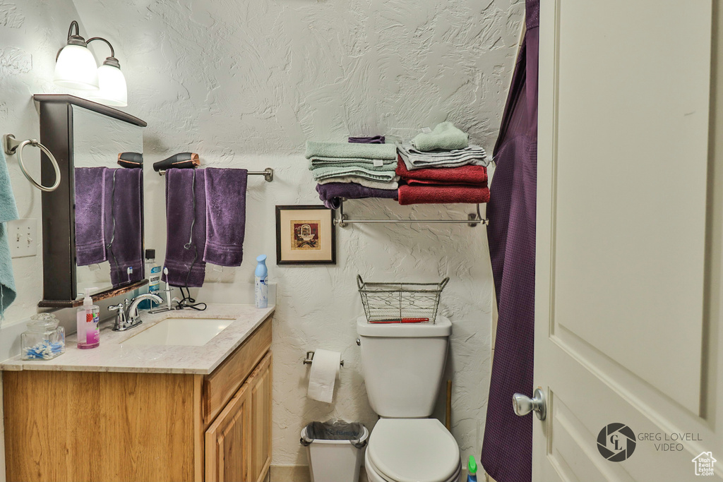 Full bathroom featuring vanity, toilet, and a textured wall