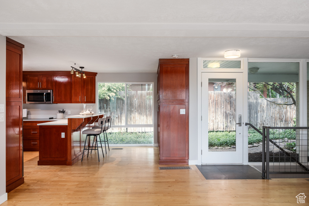 Kitchen featuring stainless steel microwave, light wood-style floors, a breakfast bar area, and dark brown cabinets