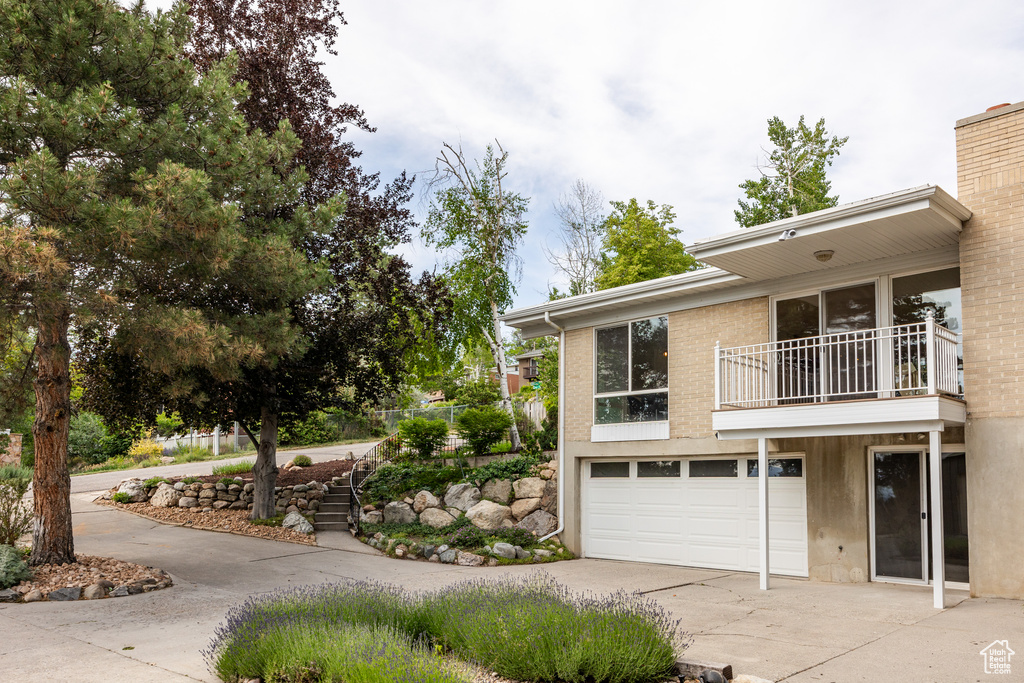 View of side of home with a balcony, driveway, a garage, and stairway