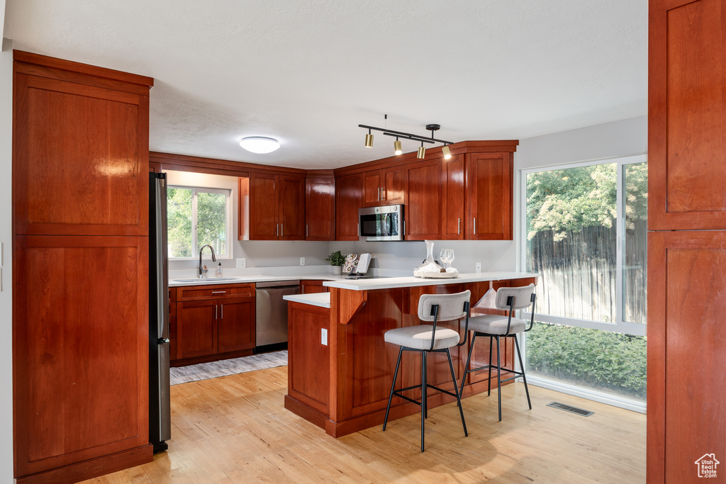 Kitchen featuring appliances with stainless steel finishes, light wood-type flooring, a breakfast bar area, light countertops, and a sink