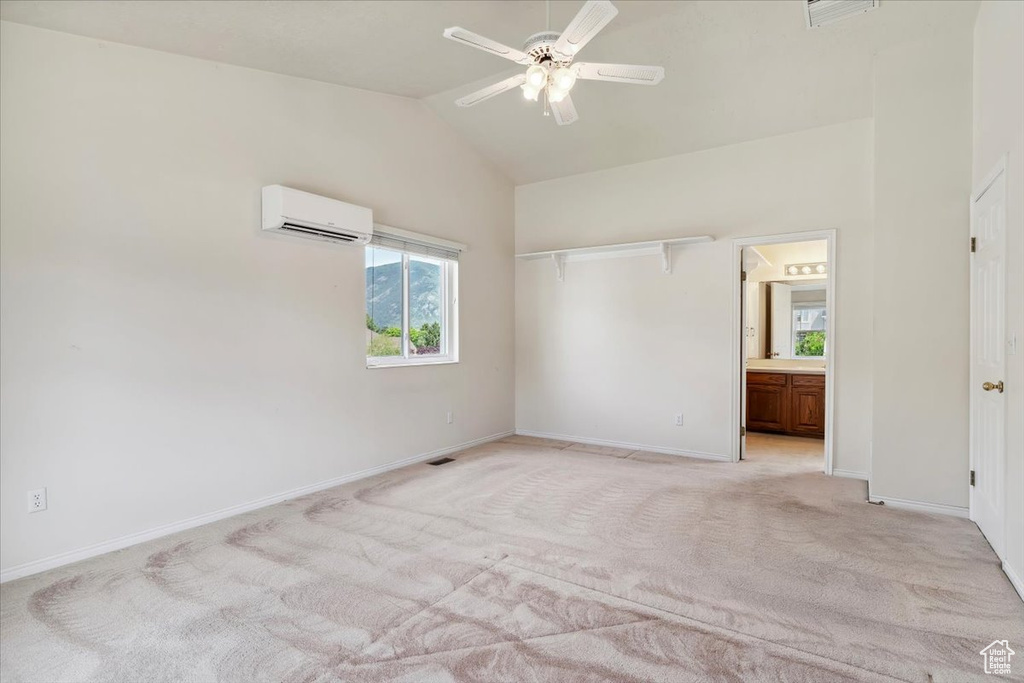 Unfurnished bedroom featuring a wall unit AC, light carpet, baseboards, high vaulted ceiling, and ensuite bathroom
