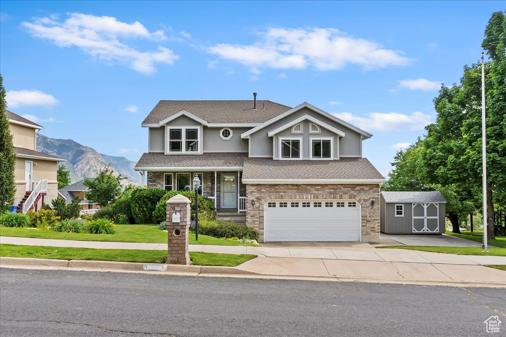 Traditional-style house featuring a garage, a mountain view, concrete driveway, a front yard, and roof with shingles