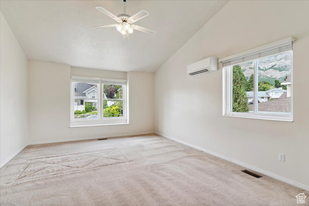 Empty room featuring a wall unit AC, ceiling fan, carpet flooring, lofted ceiling, and baseboards