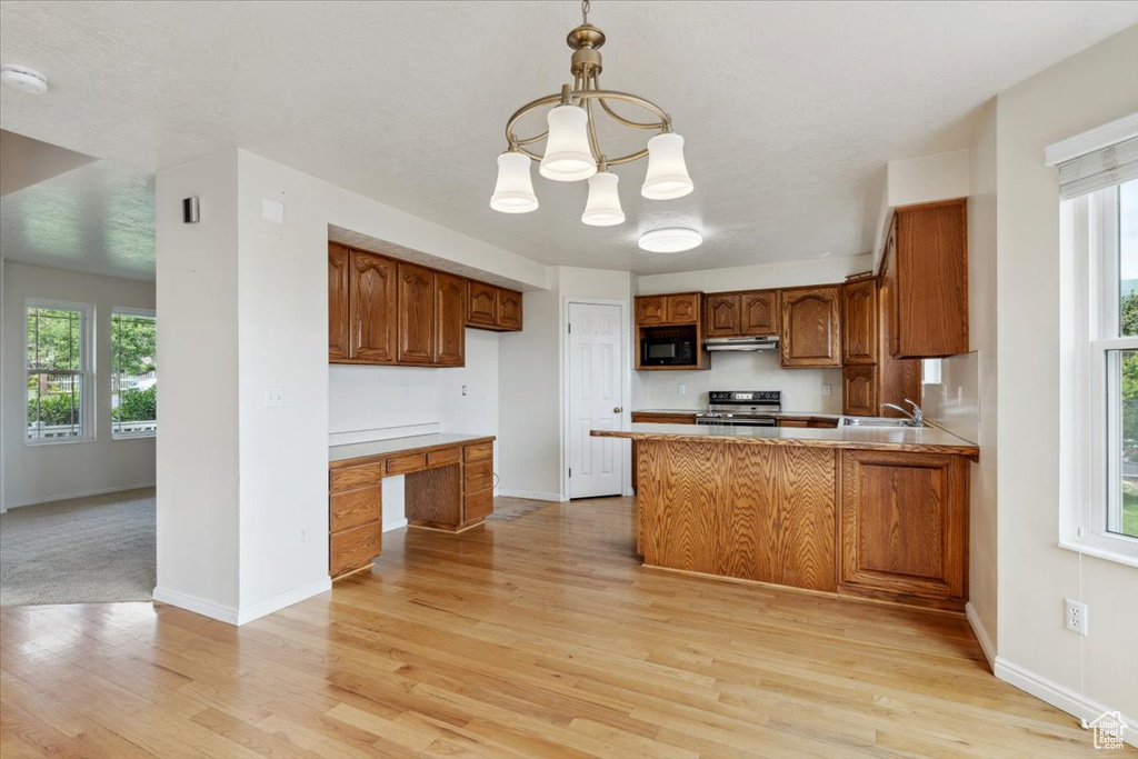 Kitchen with electric stove, black microwave, brown cabinetry, and light wood-type flooring