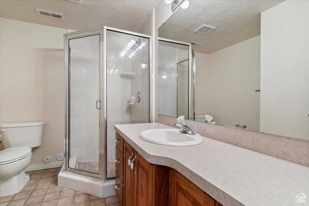 Full bath with toilet, vanity, a shower stall, tile patterned flooring, and a textured ceiling