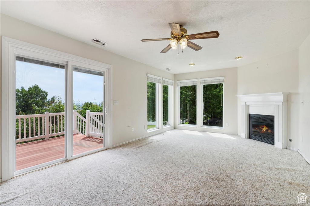Unfurnished living room featuring carpet flooring, baseboards, a ceiling fan, and a glass covered fireplace