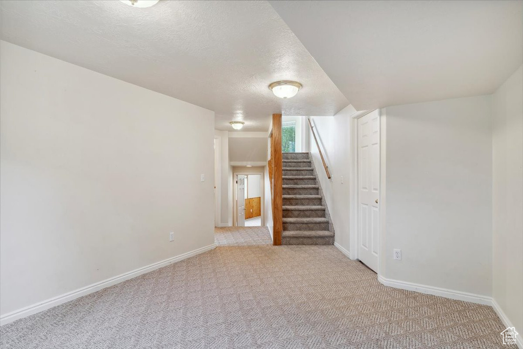 Basement with carpet floors, stairs, a textured ceiling, and baseboards