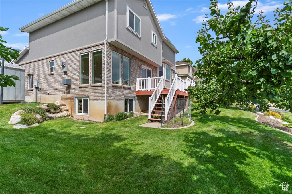 Back of house featuring stairs, a deck, brick siding, a yard, and stucco siding