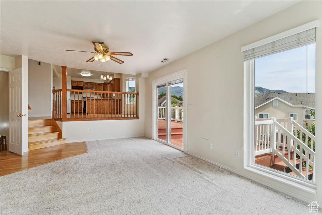 Unfurnished living room featuring carpet, a ceiling fan, stairway, and baseboards