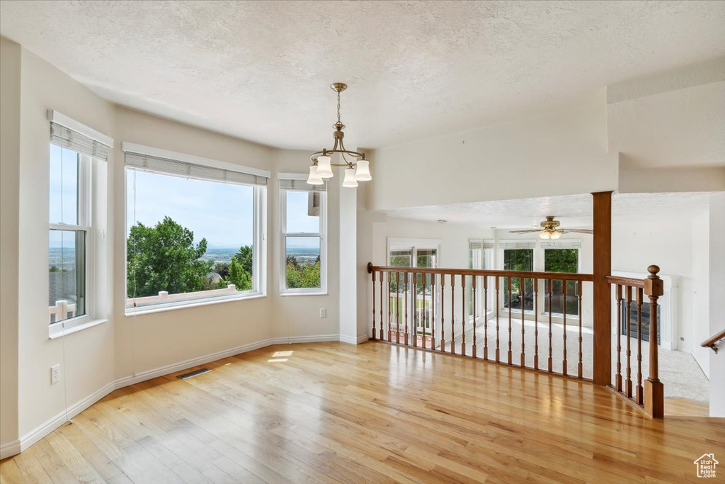 Spare room featuring a chandelier, hardwood / wood-style flooring, a textured ceiling, a ceiling fan, and baseboards