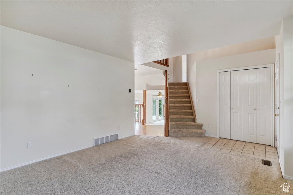 Unfurnished living room featuring carpet flooring, stairway, baseboards, and a ceiling fan