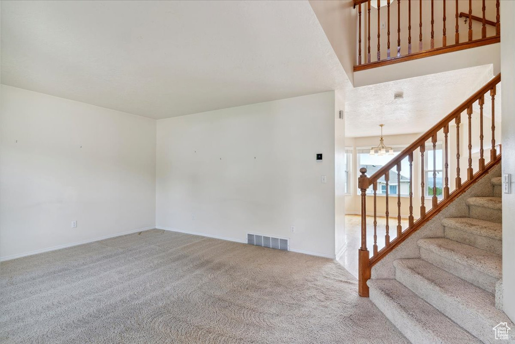 Unfurnished living room with carpet floors, stairs, a chandelier, and baseboards