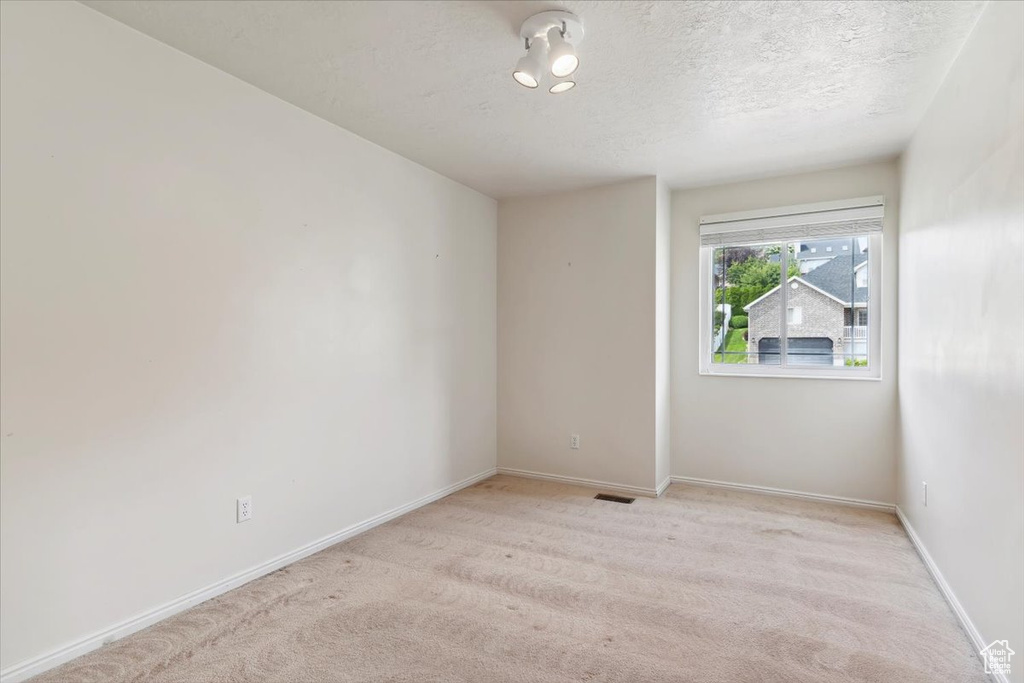 Empty room featuring a textured ceiling, light carpet, and baseboards
