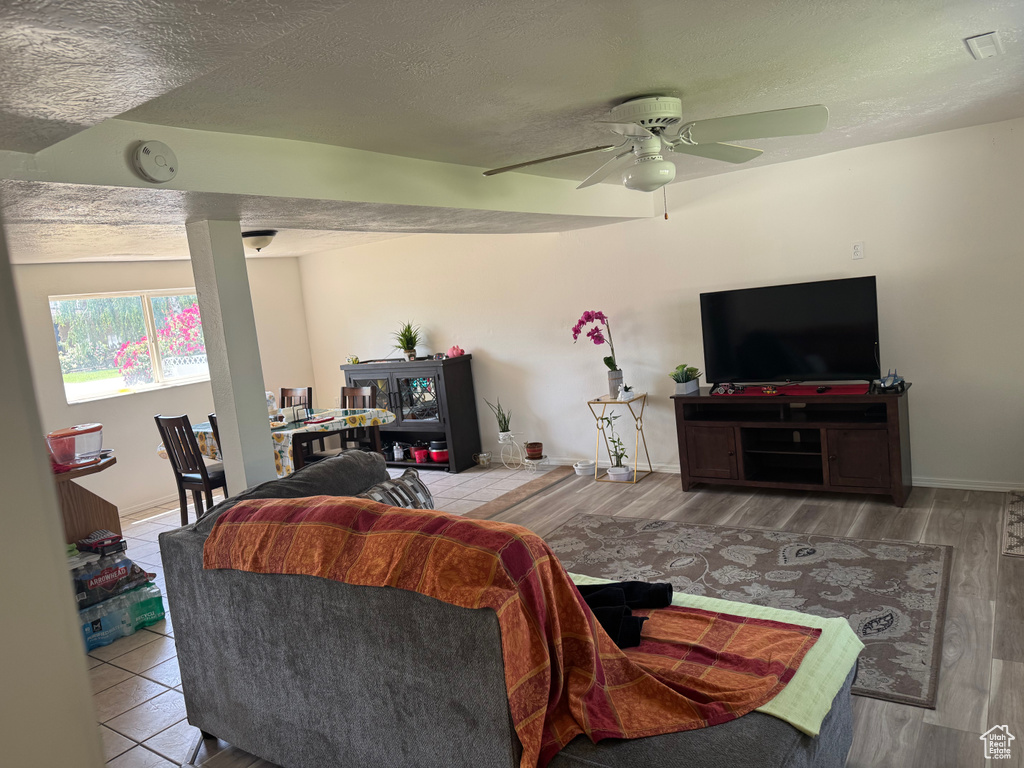 Living room with ceiling fan, wood finished floors, a textured ceiling, and baseboards