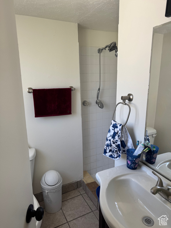 Full bathroom with toilet, tiled shower, a sink, tile patterned flooring, and a textured ceiling