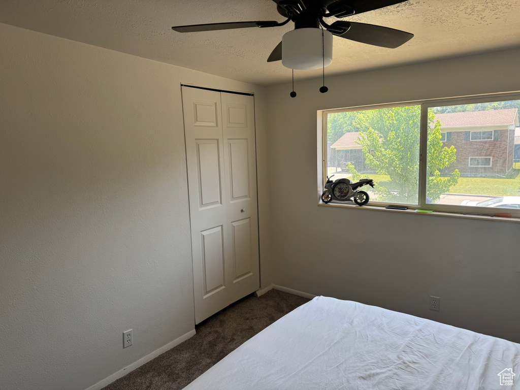 Bedroom featuring dark colored carpet, baseboards, a ceiling fan, a textured ceiling, and a closet