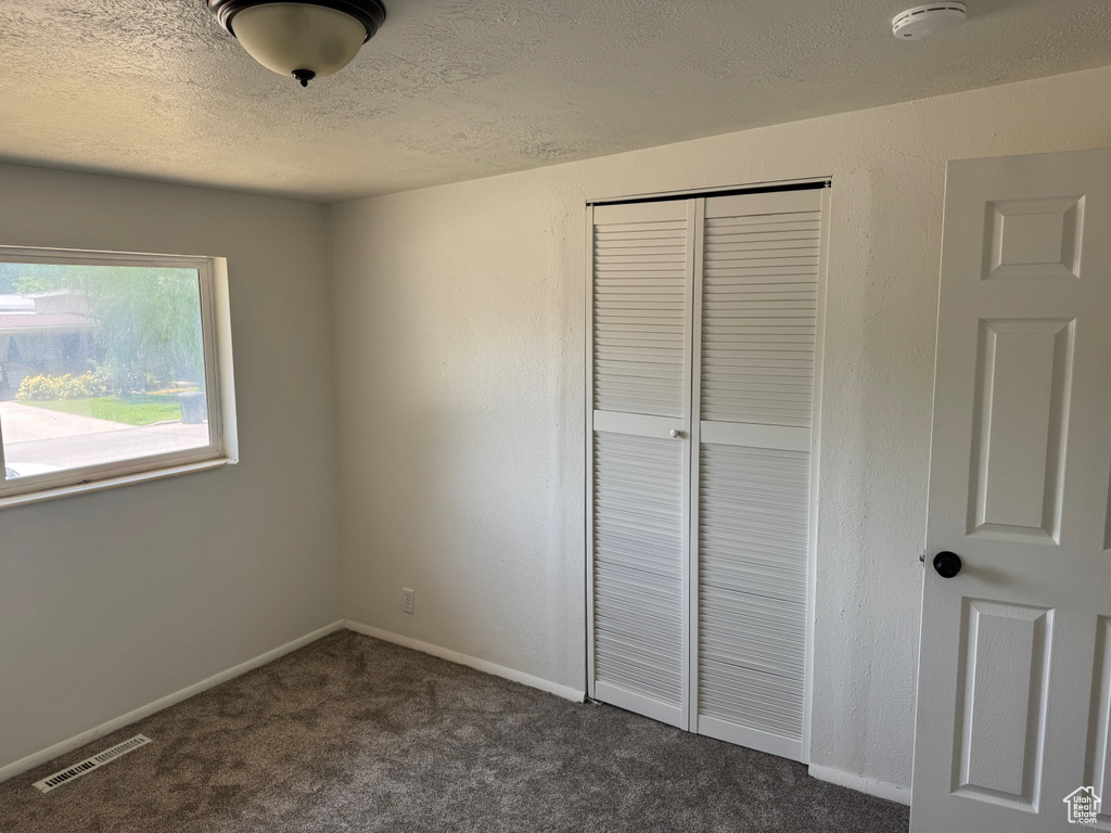 Unfurnished bedroom with a closet, a textured ceiling, dark carpet, and baseboards
