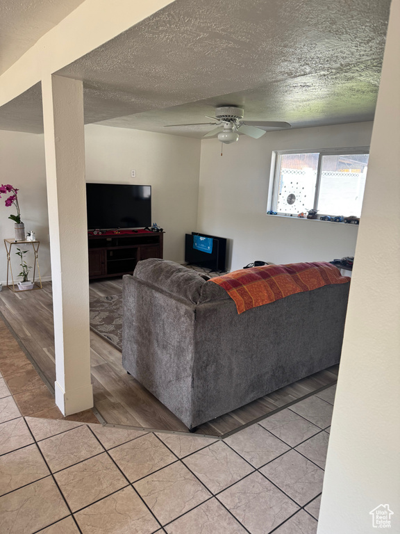 Living room featuring a textured ceiling, ceiling fan, and light tile patterned flooring