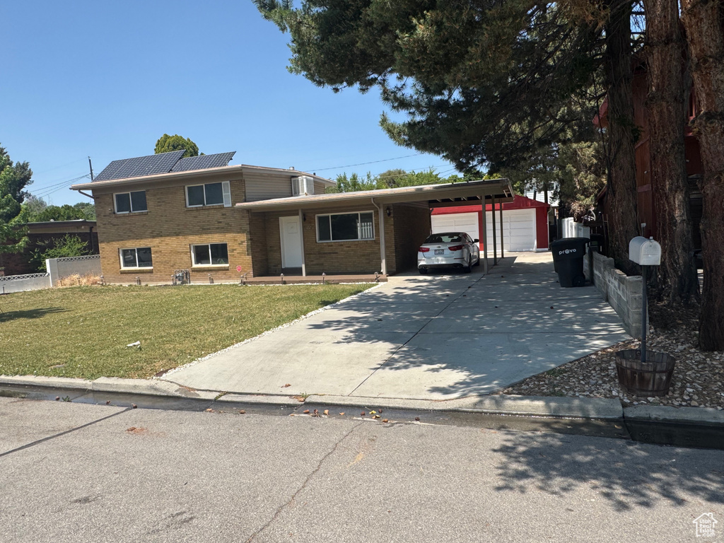Split level home featuring a carport, a front yard, brick siding, roof mounted solar panels, and concrete driveway
