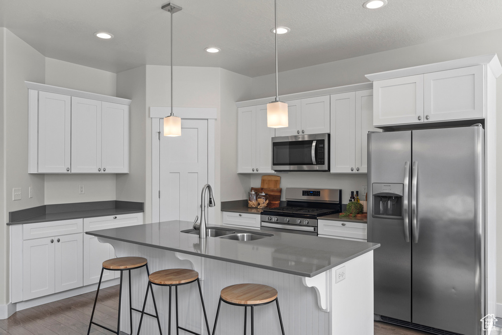 Kitchen featuring stainless steel appliances, a sink, dark countertops, white cabinetry, and a kitchen breakfast bar