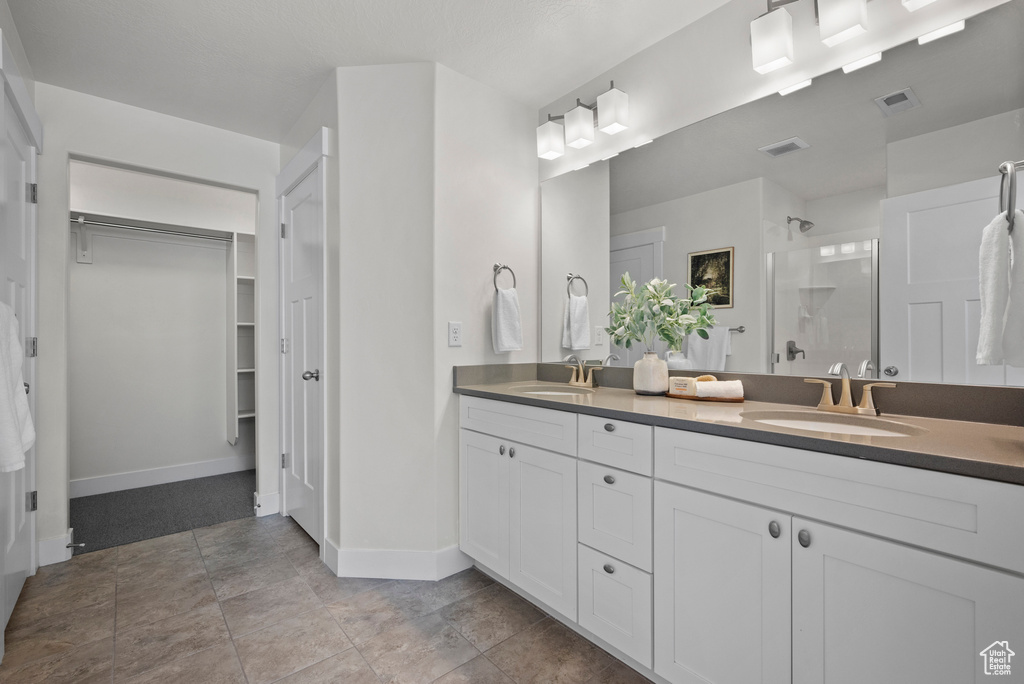Full bathroom with a shower stall, a spacious closet, double vanity, and baseboards