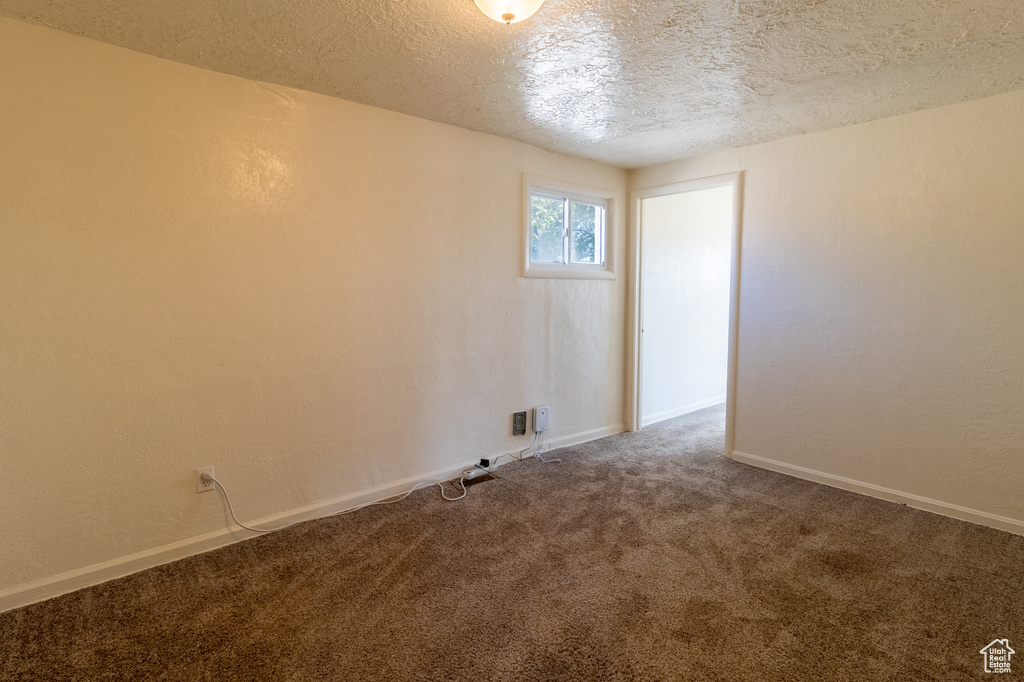 Carpeted empty room with a textured ceiling and baseboards