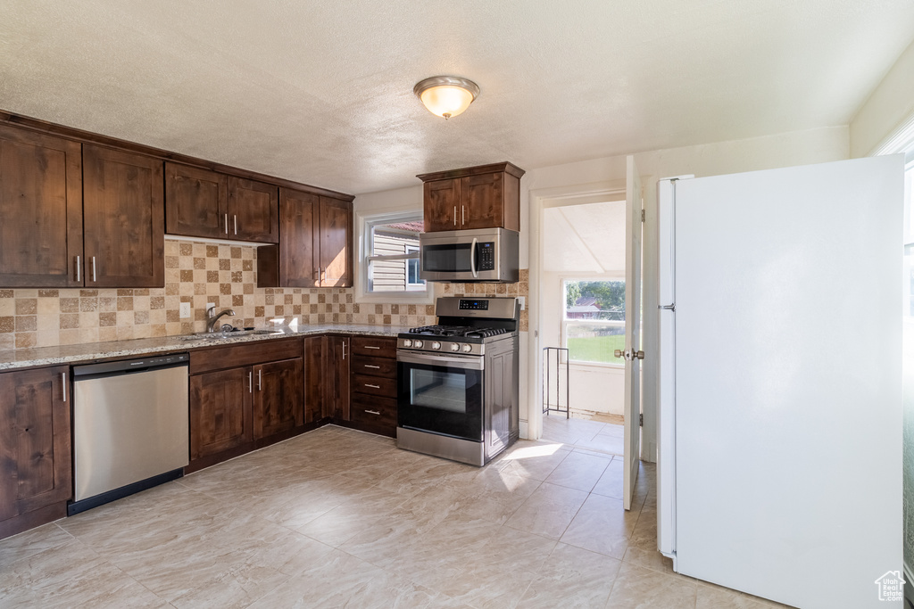 Kitchen featuring stainless steel appliances, tasteful backsplash, light stone countertops, and dark brown cabinetry