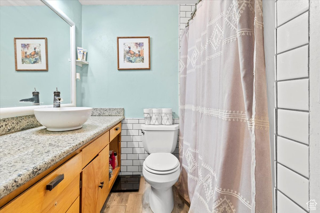 Full bath with vanity, tile walls, toilet, wood finished floors, and a shower with shower curtain