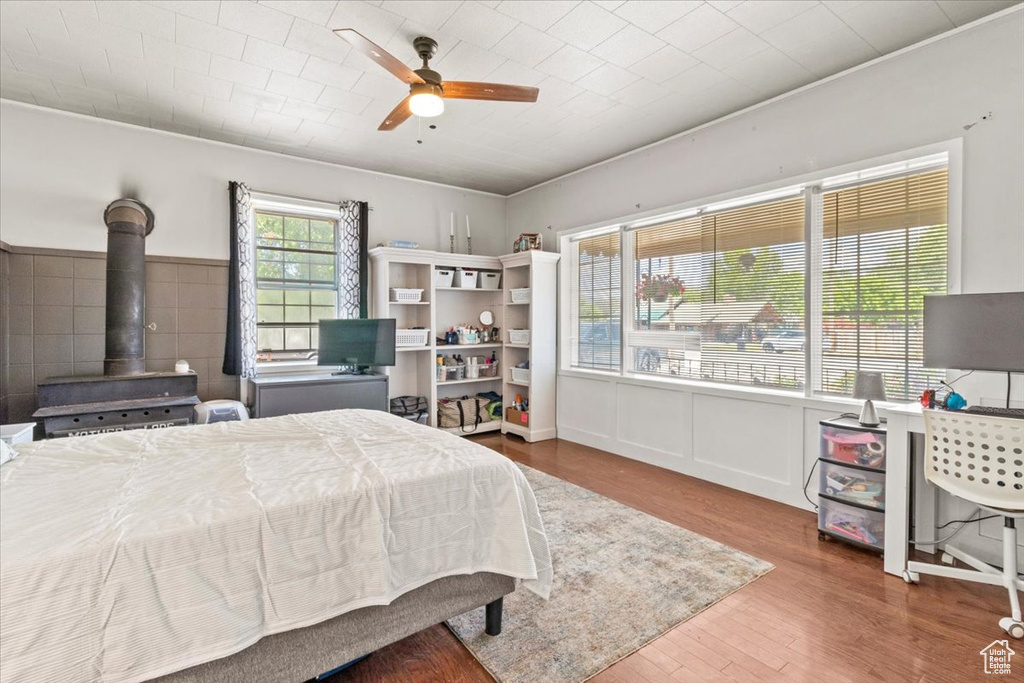 Bedroom with a wood stove, wood finished floors, and ceiling fan