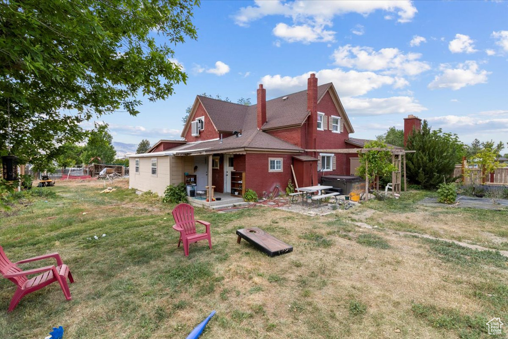 Back of property with a hot tub, a patio, a chimney, and brick siding