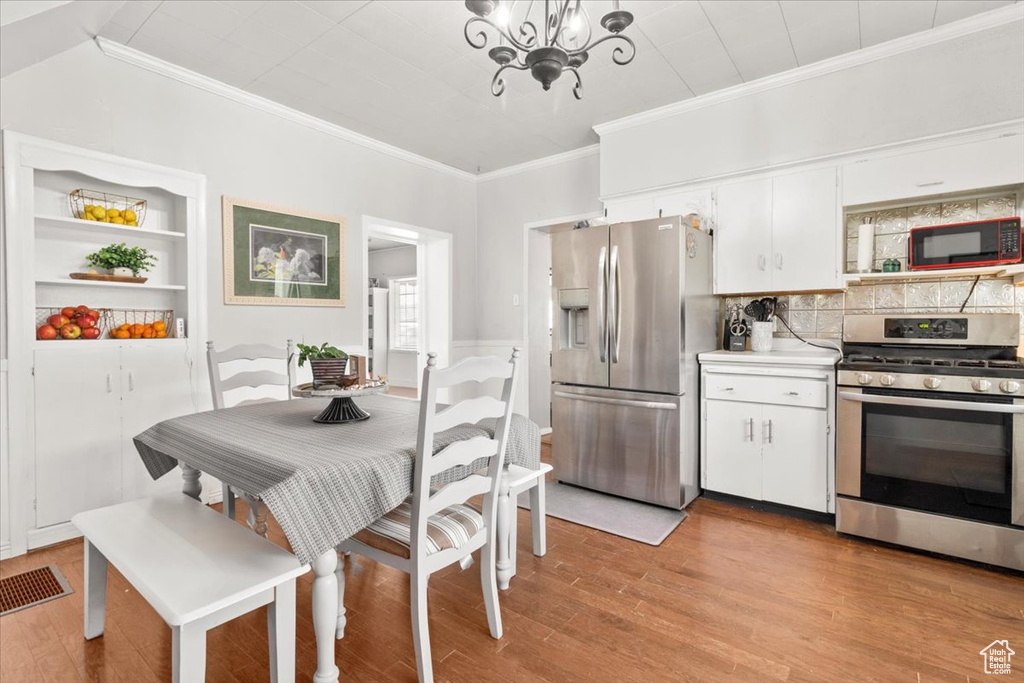 Kitchen with stainless steel appliances, crown molding, a chandelier, light wood-style floors, and white cabinets