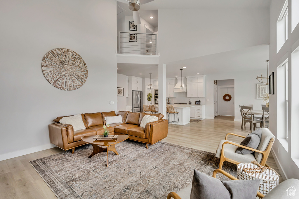 Living room featuring a towering ceiling, light wood-style floors, recessed lighting, baseboards, and plenty of natural light