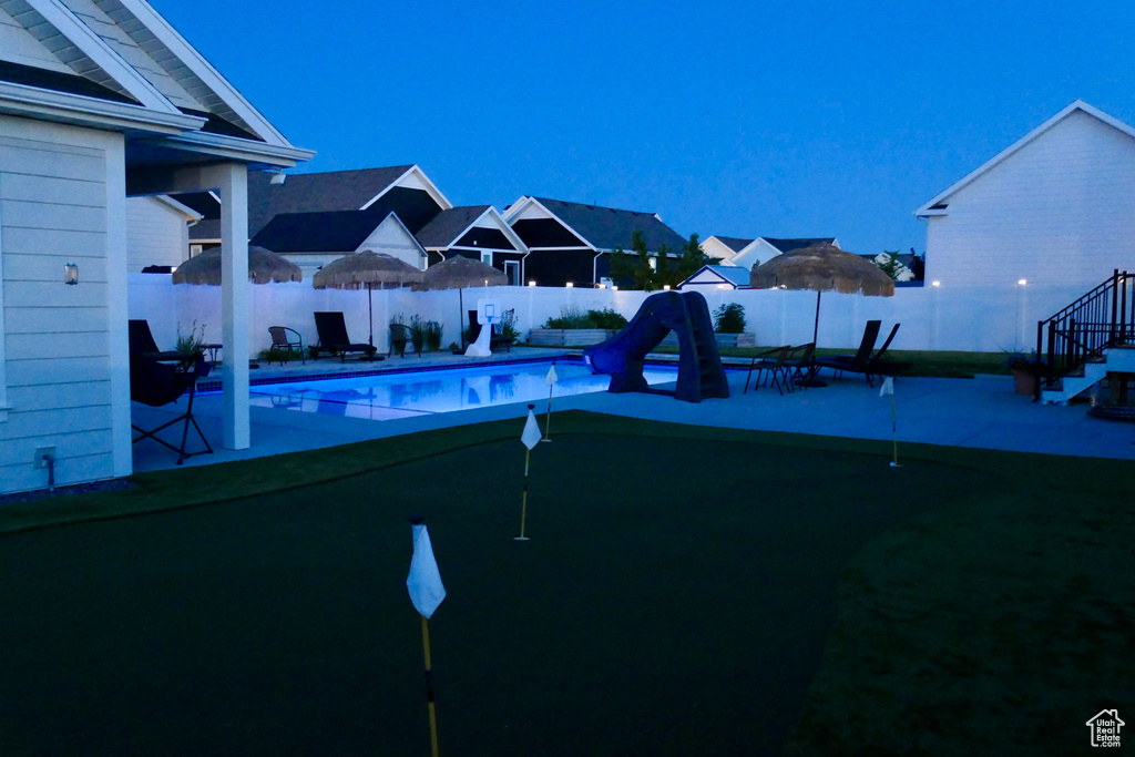 View of pool with a putting area, a water slide, a fenced backyard, and a patio